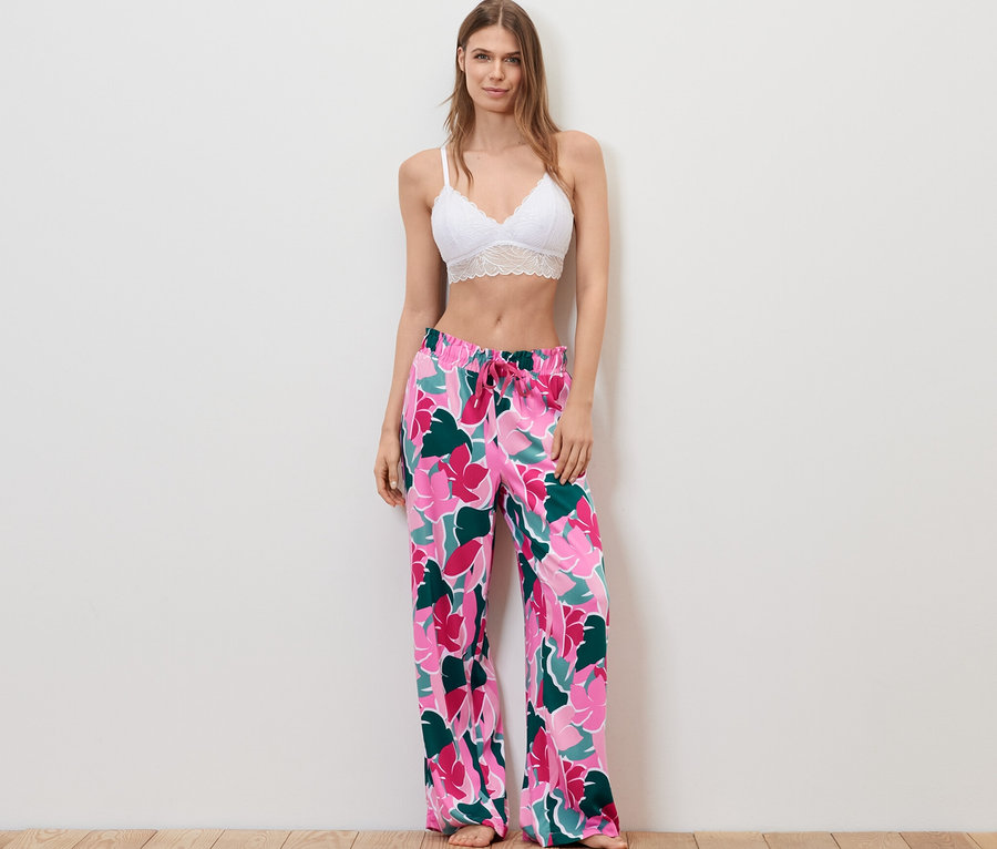 Frau steht und trägt einen weißen Spitzen-BH und eine Relaxhose mit Blumenmuster.