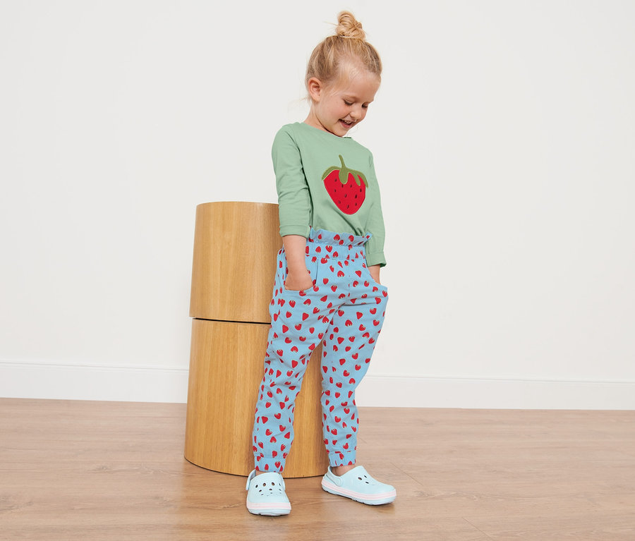 Mädchen trägt eine Kleinkinder-Paperbaghose mit Erdbeer-Alloverprint.