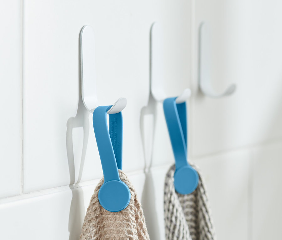 Zwei Handtücher hängen mit blauen 2 Magnet-Clips an weißen Haken an weißen Fliesen.