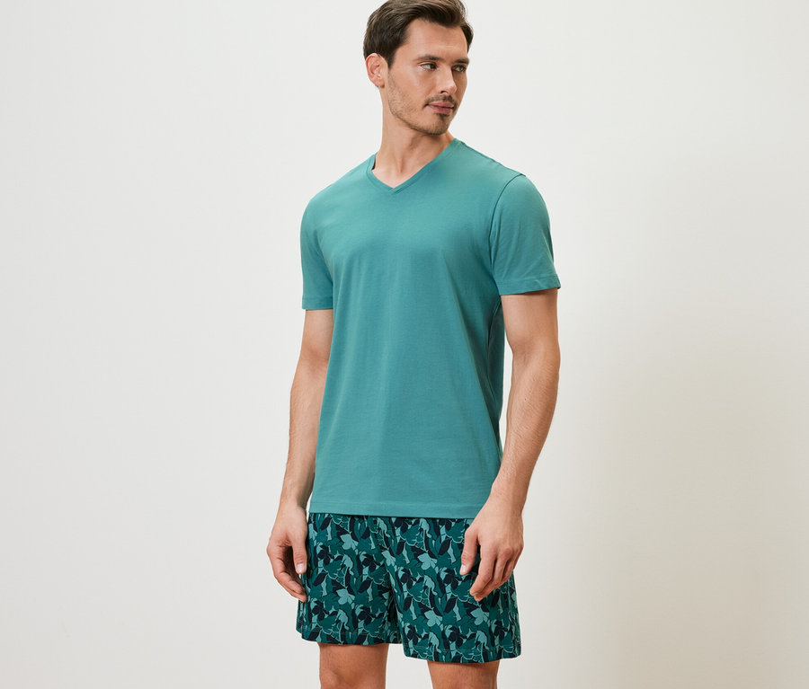 Mann trägt ein Shorty-Pyjama-Set mit einem kurzärmeligen Oberteil und bedruckten Shorts.