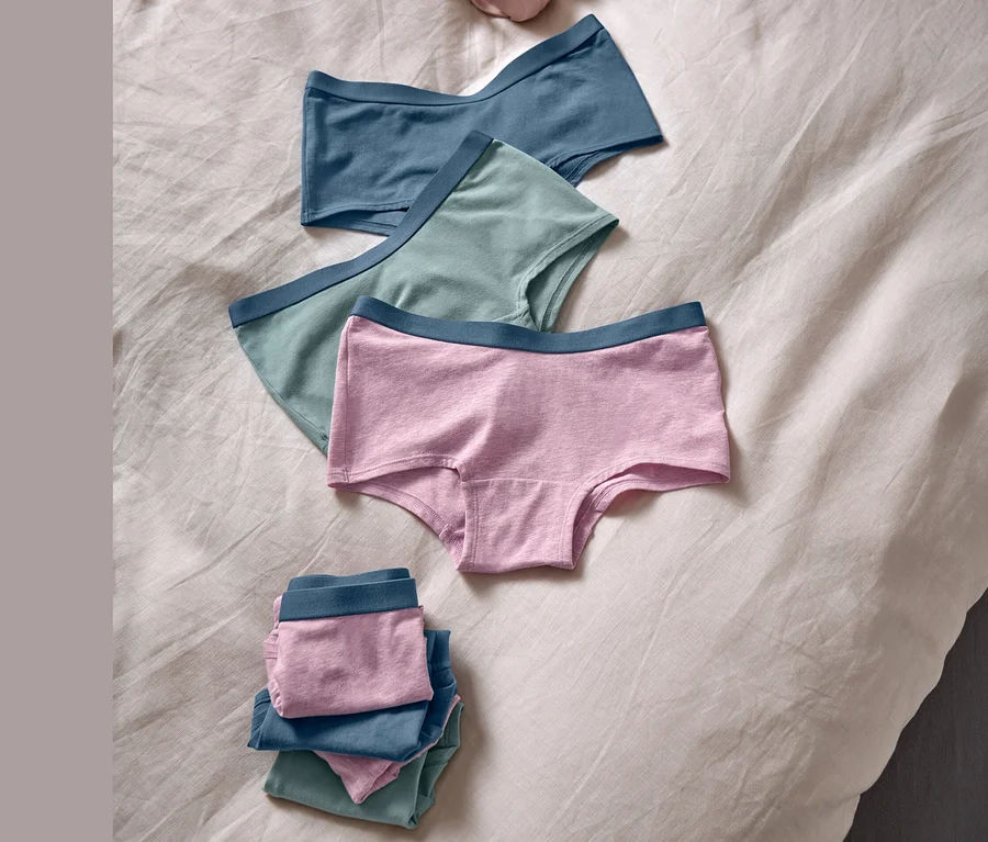 Auf einem Bett liegen 7 Mädchen-Pantys und rosafarbene Kopfhörer.