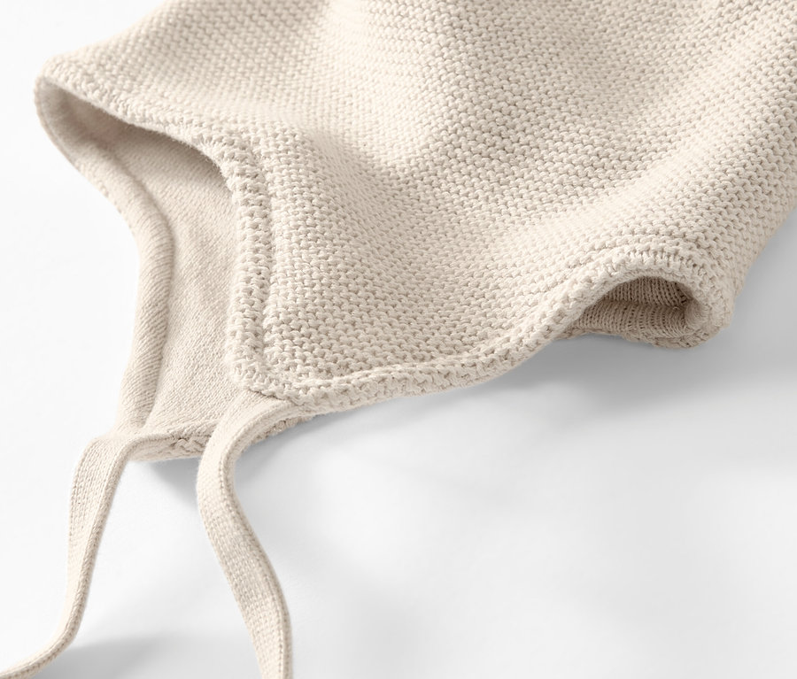 Detailansicht einer cremefarbenen Baby-Strickmütze und eines Strickschals auf weißem Hintergrund.