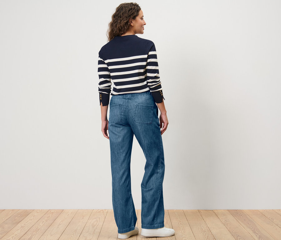 Eine Frau steht mit dem Rücken zur Kamera und trägt eine Wide-Comfort-Jeans und ein gestreiftes Oberteil.