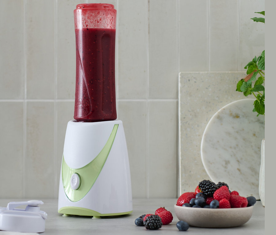 Smoothie-Maker mit rotem Smoothie und einer Schüssel mit Beeren.