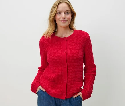 Frau posiert in rotem Cardigan aus Strukturstrick und blauen Jeans.