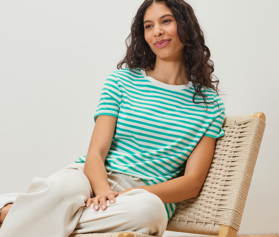 Frau sitzt auf Stuhl mit einem aqua-weiß gestreiften Basic T-Shirt.