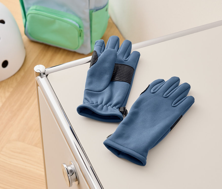 Blaue Handschuhe liegen auf einem weißen Schrank, im Hintergrund ein Rucksack und ein Helm.