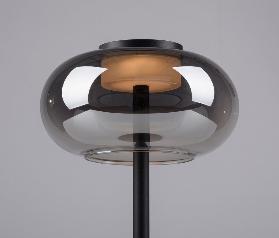 Detailaufnahme einer schwarzen Lampe mit einem rauchfarbenen Glasschirm, der warmes Licht ausstrahlt.