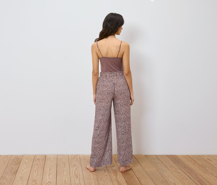 Eine Frau steht mit dem Rücken zum Betrachter und trägt ein braunes Tanktop und eine locker sitzende Hose mit Animal-Print.