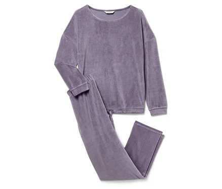 Ein lilafarbener Velours-Pyjama mit langen Ärmeln und Hosen liegt auf einem weißen Hintergrund.