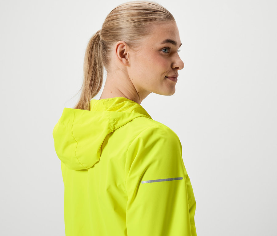 Frau mit blonden, zum Pferdeschwanz gebundenen Haaren, trägt eine neongelbe Jacke mit Kapuze.