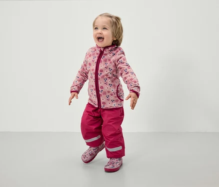 Kleinkind in rosa Fleecejacke mit Blumenmuster und rosa Hose.