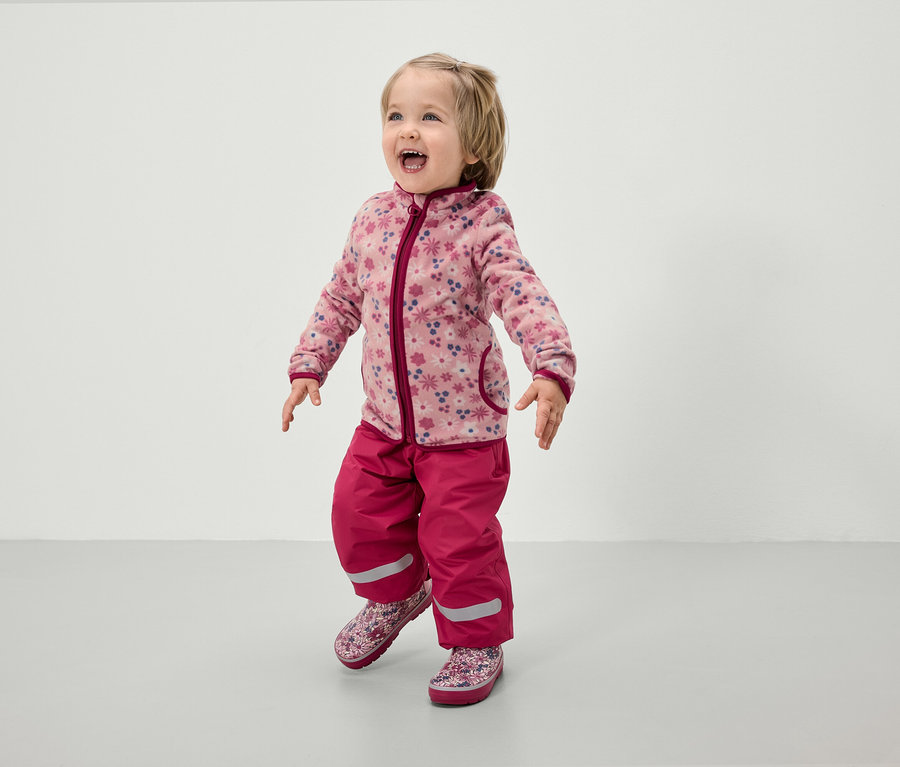 Kleinkind in rosa Fleecejacke mit Blumenmuster und rosa Hose.