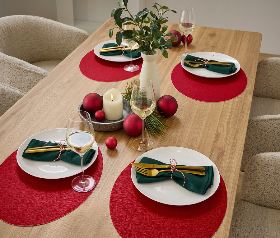 Gedeckter Tisch mit vier Gedecken mit roten Platzsets, weißen Tellern, grünen Servietten und goldenem Besteck.