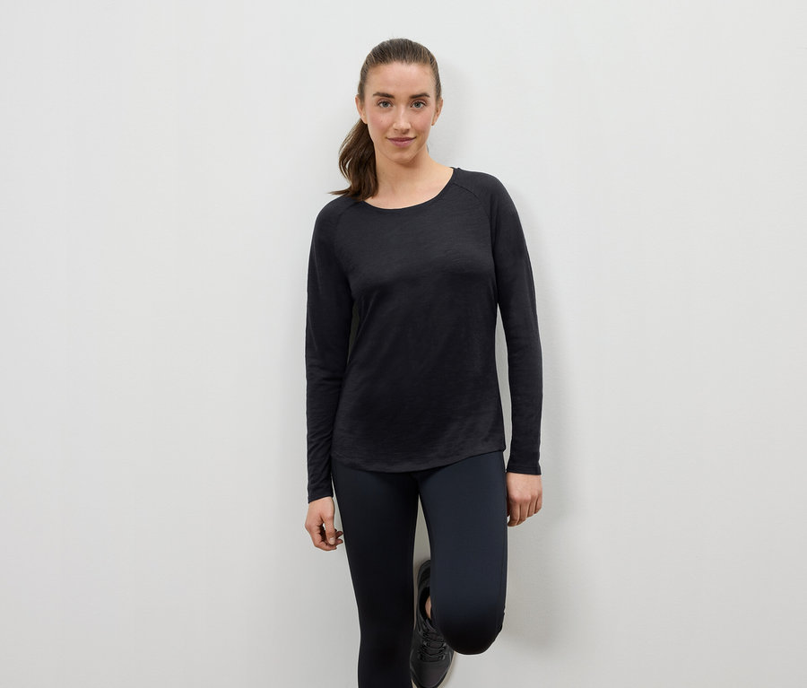 Frau in schwarzer Sportbekleidung, die sich an eine Wand lehnt.