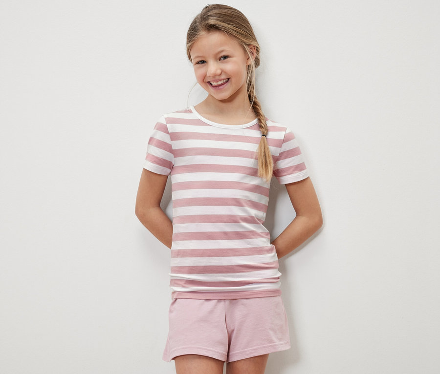 Lächelndes Mädchen posiert in einem rosa-weiß gestreiften Kinder-T-Shirt und rosa Shorts.