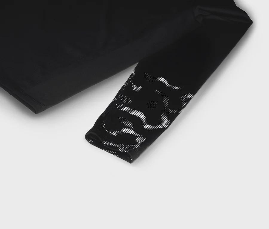 Schwarzes Langarmshirt mit weißem Punktmuster am Ärmelende, liegend auf weißem Hintergrund.