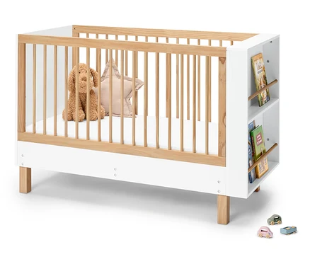 Ein Kinderbett aus Holz und Weiß mit einem Stofftierhund, einem Sternkissen und Büchern an der Seite.