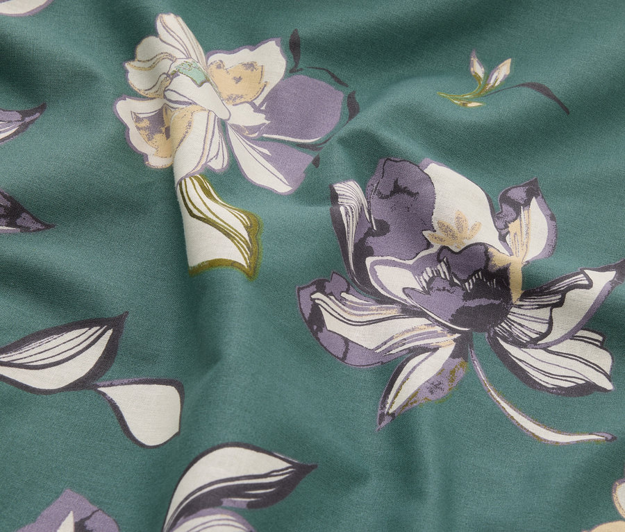 Nahaufnahme eines Stoffes mit Blumenmuster in Grün-, Lila- und Cremetönen.