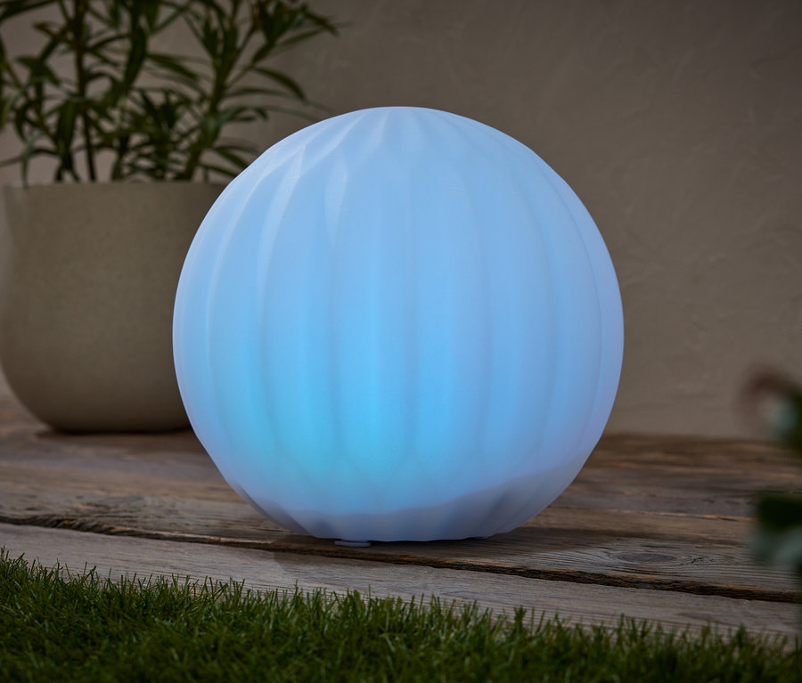 Eine blaue Kugel leuchtet auf einer hölzernen Oberfläche, neben einer Topfpflanze.