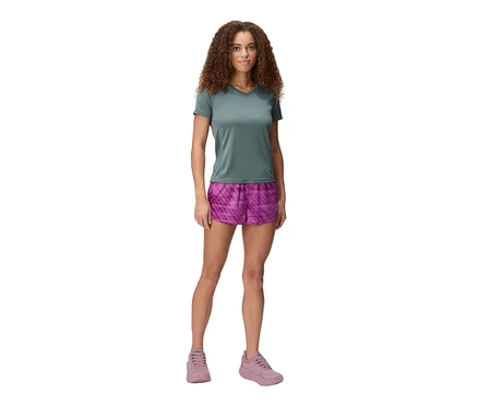 Frau steht mit grünem T-Shirt, pinken Shorts und pinken Schuhen vor weißem Hintergrund.