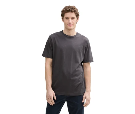 Mann mit lockigem Haar trägt ein dunkelgraues Tom Tailor T-Shirt mit Logo und dunkelblaue Hose.