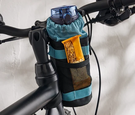 Eine blaue Trinkflasche und ein Müsliriegel befinden sich in einer am Fahrrad befestigten Halterung.