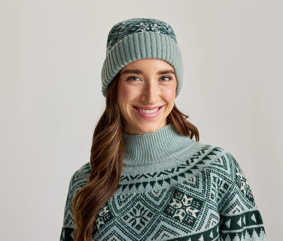 Lachende Frau mit hellgrüner Mütze und passendem gemustertem Pullover.