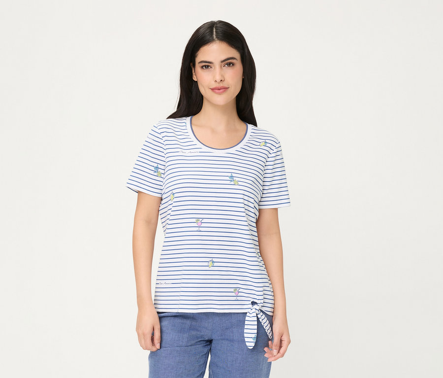 Frau trägt ein Olsen T-Shirt, ein weiß-blau gestreiftes Kurzarmshirt mit kleinen Cocktailglas- und Zitronenscheibenmotiven, links an der Hüfte gebunden, dazu blaue Hose.