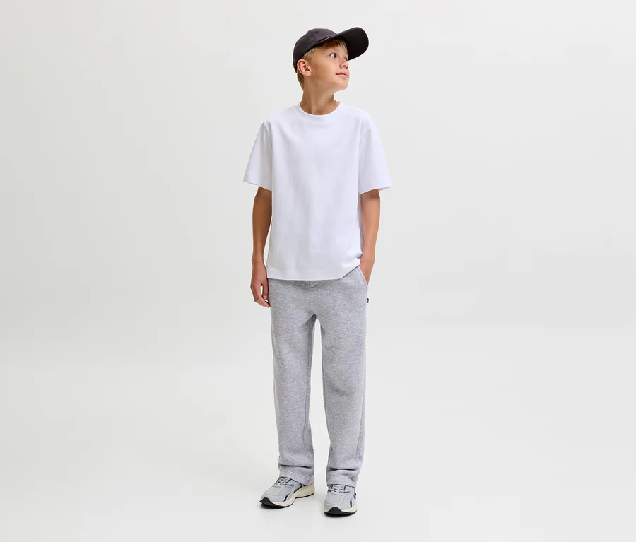 Junger Junge trägt ein weißes T-Shirt, eine dunkelgraue Baseballkappe und graue Jack&Jones Bradley Sweatpants, steht mit Händen in den Taschen und blickt nach rechts.