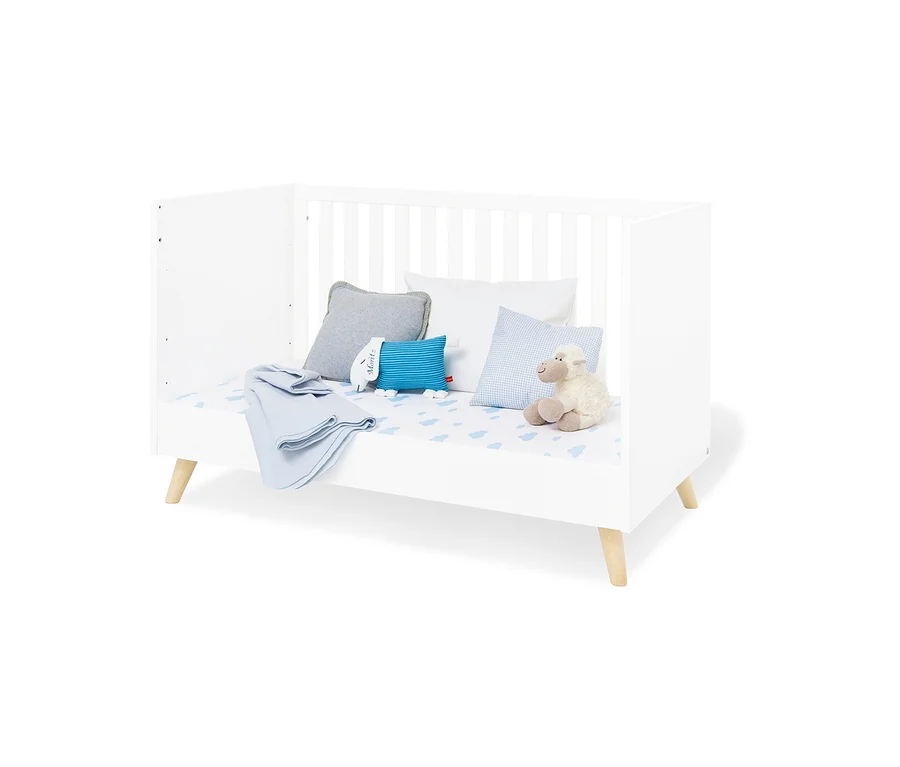 Weißes Pinolino Babybett »Move« mit blauen und weißen Kissen und einem Stoffschaf.