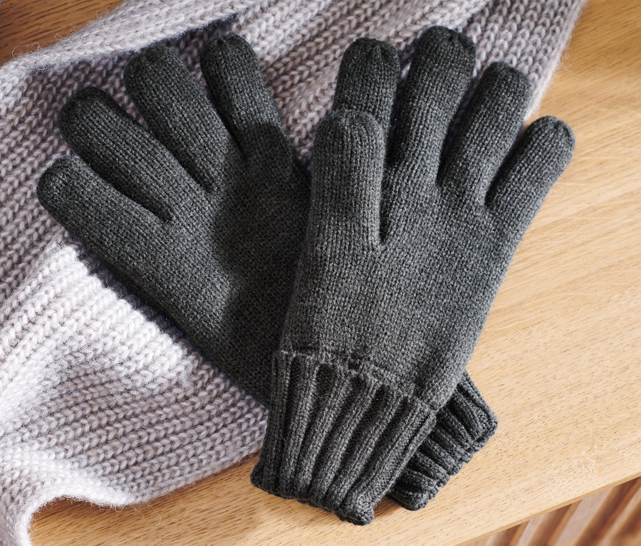 Graue Strickhandschuhe liegen auf einem grauen Strickschal auf einer Holzoberfläche.