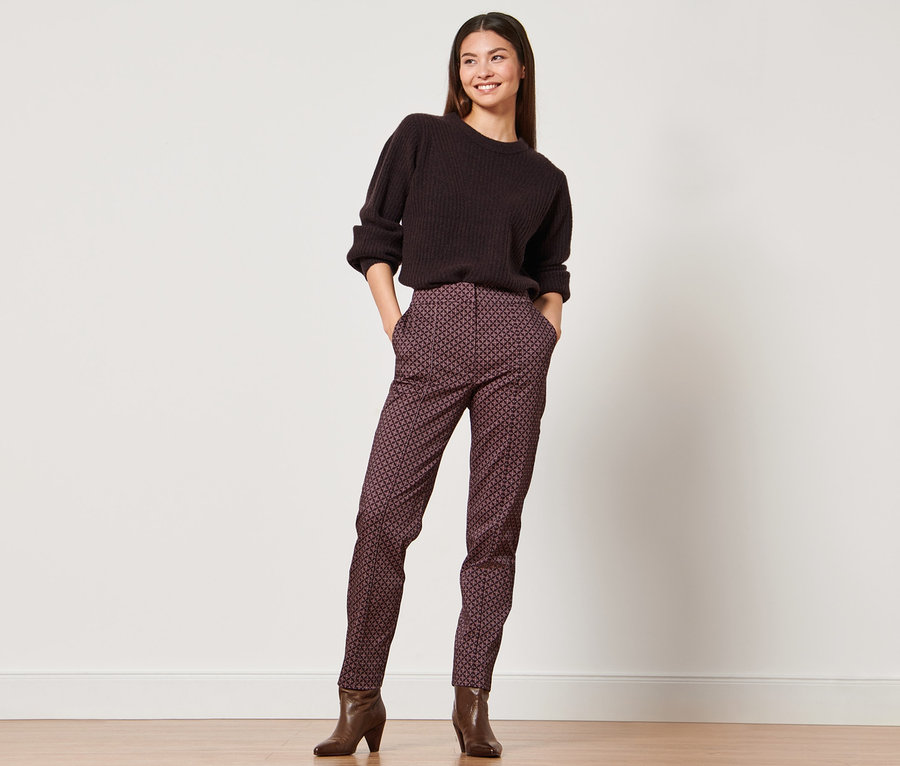 Frau posiert in braunem Pullover und Webhose.