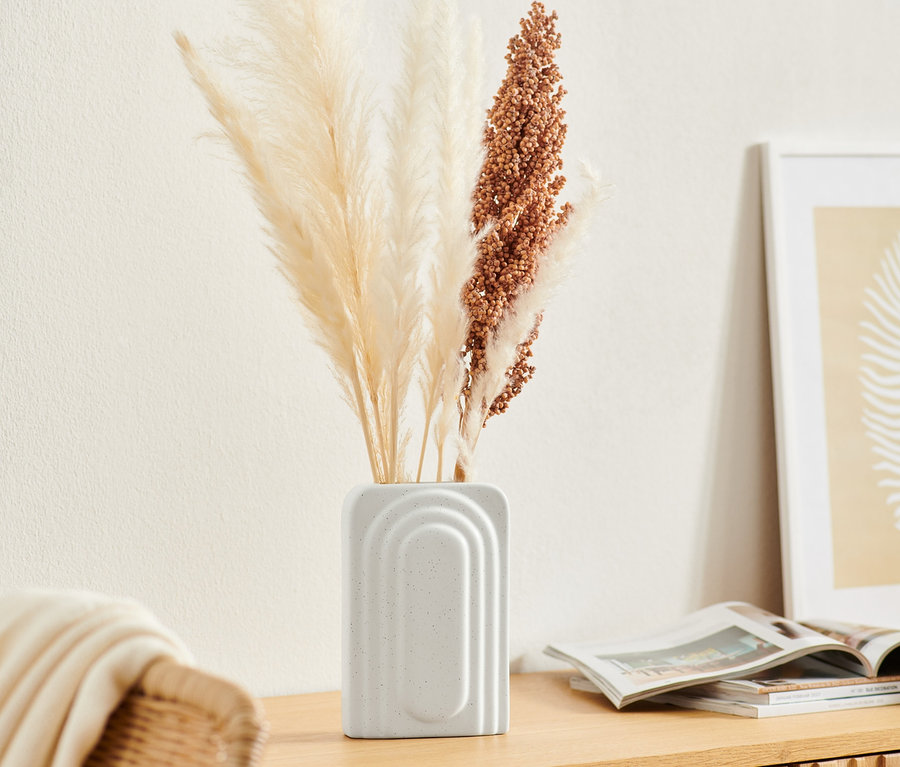 Eine kleine Vase aus Keramik mit Pampasgras steht auf einer Holzkommode.
