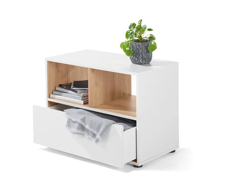 Weißes Sideboard mit Schublade, darauf eine Pflanze in einem grauen Topf. Im offenen Fach liegen Bücher, in der Schublade eine graue Decke.