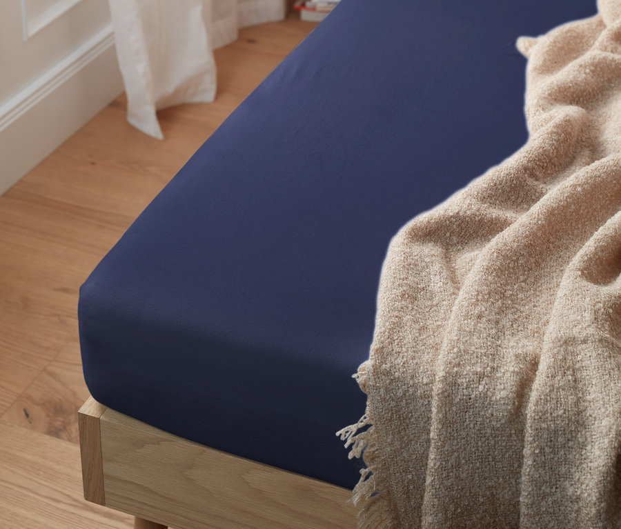 Blaues Jersey-Spannbettlaken in Normalgröße auf einem Bett mit einer beigen Decke.
