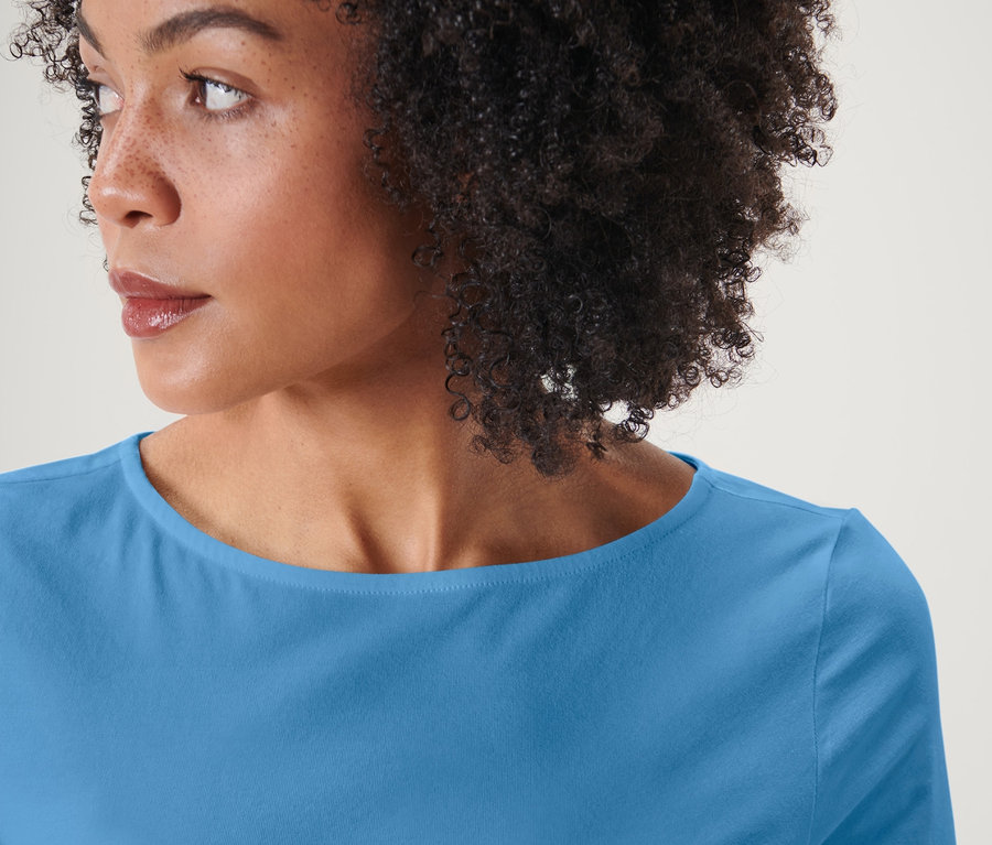 Porträt einer Frau mit Afro-Haar, die ein hellblaues Shirt mit 3/4-Arm trägt.