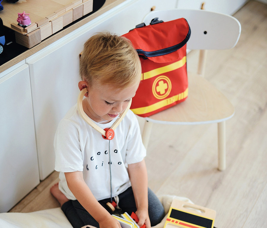 Ein Junge spielt mit einem Teddybär und einem Arztkoffer, trägt ein Stethoskop und daneben liegt ein small foot Notarzt-Rucksack.