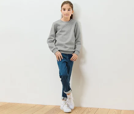 Mädchen lehnt an einer weißen Wand und trägt ein graues Kinder-Sweatshirt mit angerauter Innenseite.
