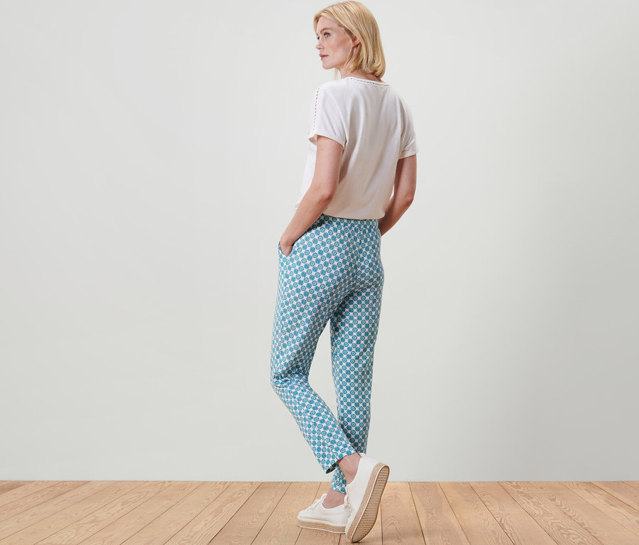 Blonde Frau steht mit dem Rücken zur Kamera und trägt eine Jerseyhose mit Alloverprint.