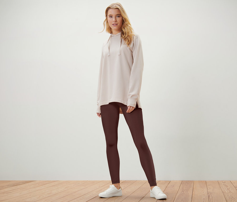 Blonde Frau posiert in hellbeigem Hoodie und braunen 2 Leggings.
