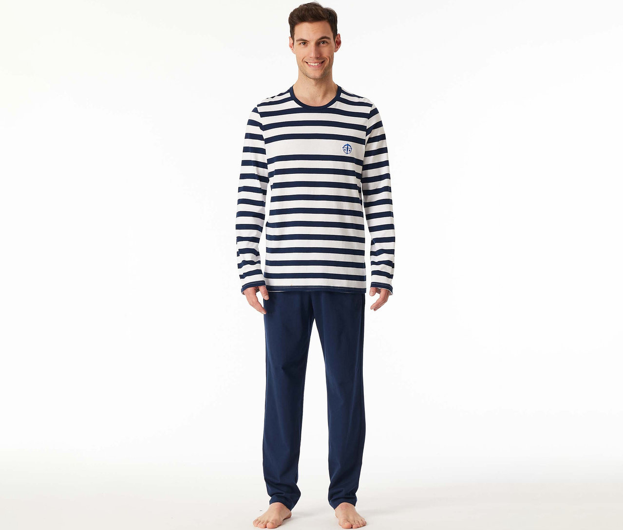 Lächelnder Mann trägt ein SCHIESSER Pyjama-Set mit einem weiß-marineblau gestreiften Langarmshirt mit Anker-Emblem und einer marineblauen Hose.