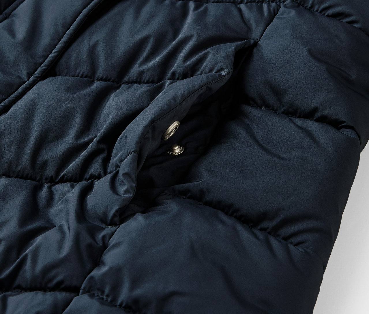 Detailaufnahme einer dunkelblauen Steppjacke mit Kapuze und Tasche.