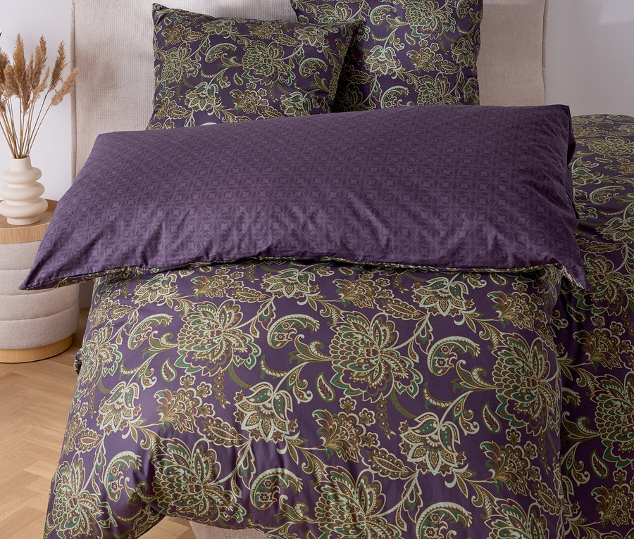 Ein Bett mit lila Bettwäsche mit Blumenmuster und zwei Kissen.