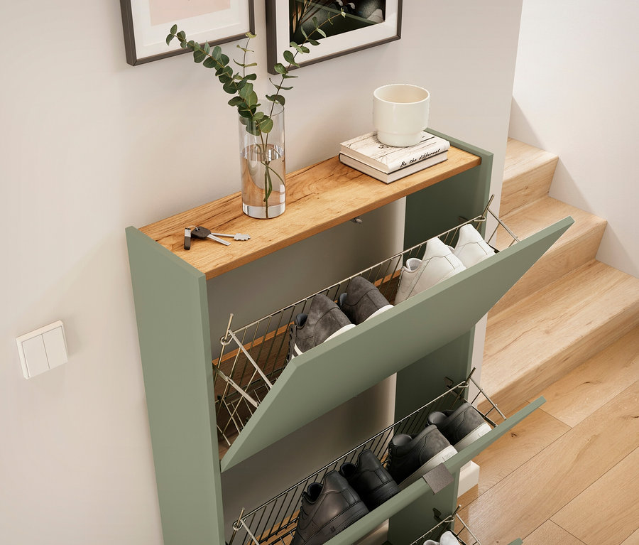 Ein grüner Schuhschrank mit einer Holzplatte, auf der Schlüssel, eine Vase mit einer Pflanze, ein Buch und eine weiße Tasse liegen.
