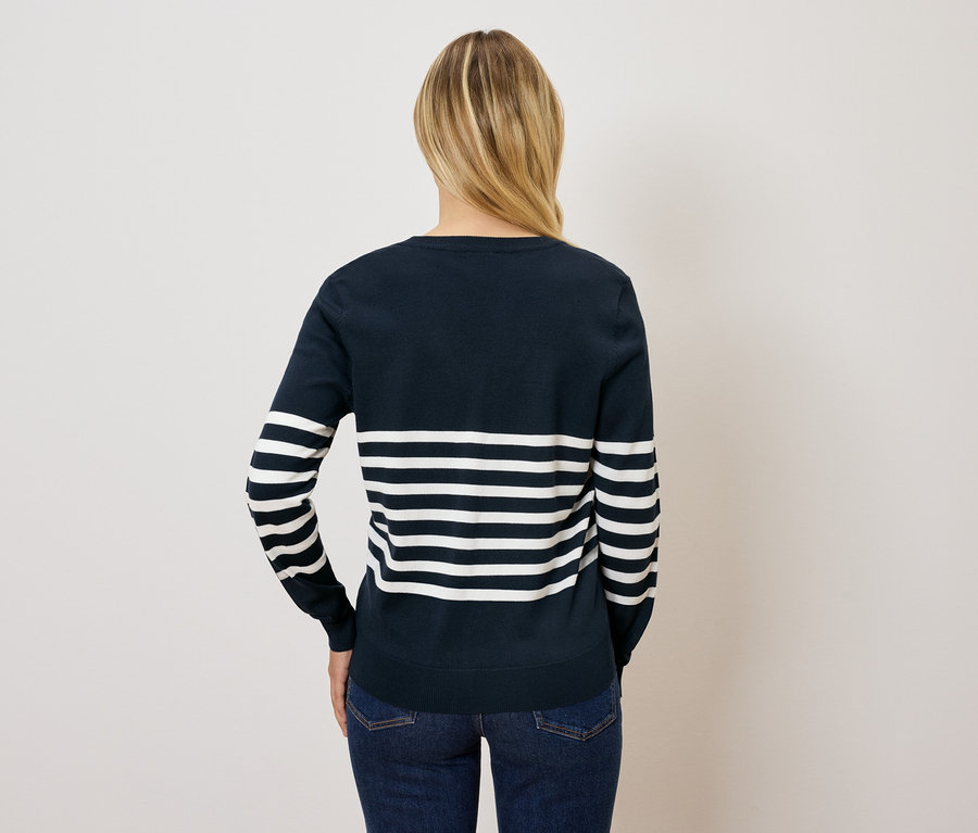 Von hinten ist eine Frau mit blonden Haaren in einem blau-weiß gestreiften Pullover und Jeans zu sehen.