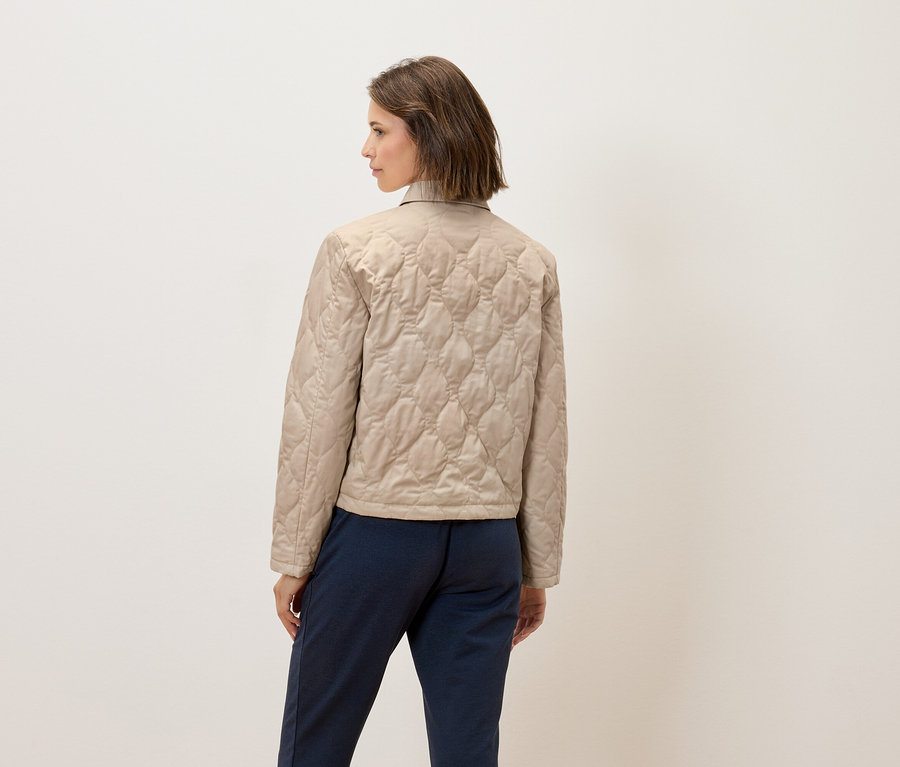 Frau mit dem Rücken zur Kamera trägt eine beige Steppjacke und blaue Hosen.