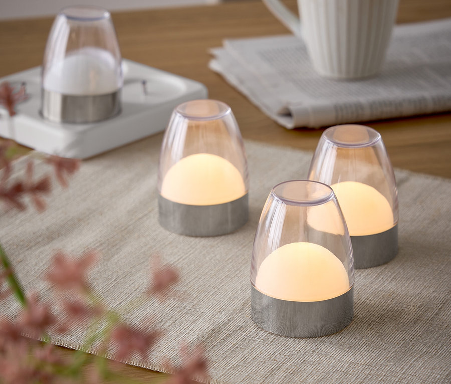 Vier Lampen auf einem Tisch mit Tischdecke, neben einer Tasse und einer Zeitung.