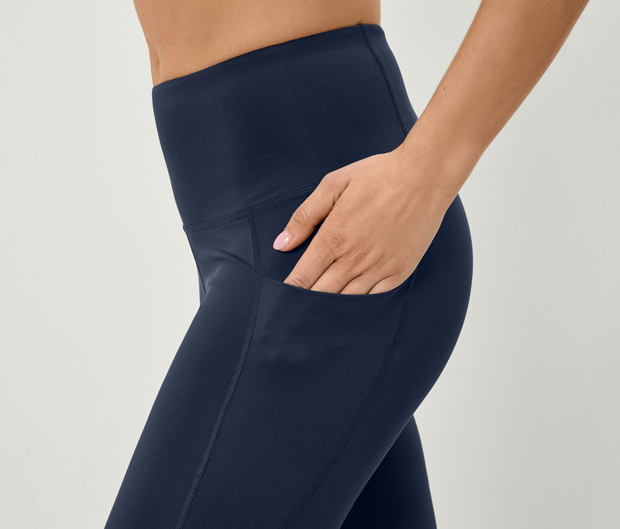 Frau steckt Hand in die Tasche einer dunkelblauen Leggings.