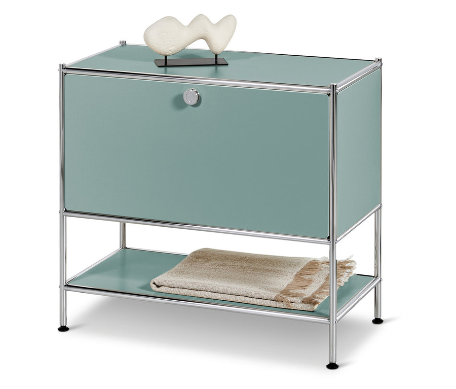 Türkisfarbener Schrank mit Chromrahmen, darauf eine weiße Dekoration, darunter eine Decke.